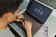 A man working on a laptop with AI software open on the screen, wearing eyeglasses.
